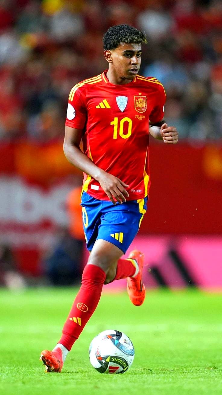 IPTV Gen A male soccer player in a red and yellow Spain jersey with the number 10 dribbles a ball on the field during a match, broadcast live on IPTV Latino. The background shows a blurred crowd.
